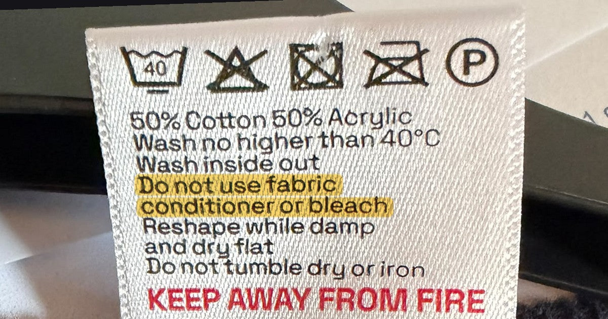 Care label on a child’s school jumper, with “Do not use fabric conditioner or bleach” highlighted and “Keep away from fire” in red at the bottom
